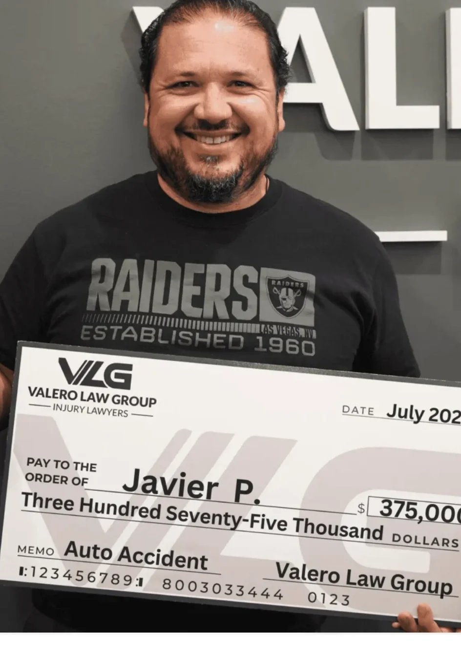 Valero Law Group client Javier P. holding a $375,000 auto accident settlement check
